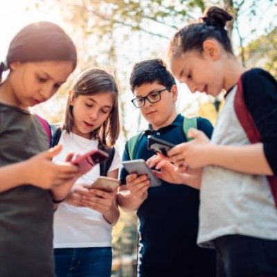 Four adolescents standing in a group, looking on their smart phones.